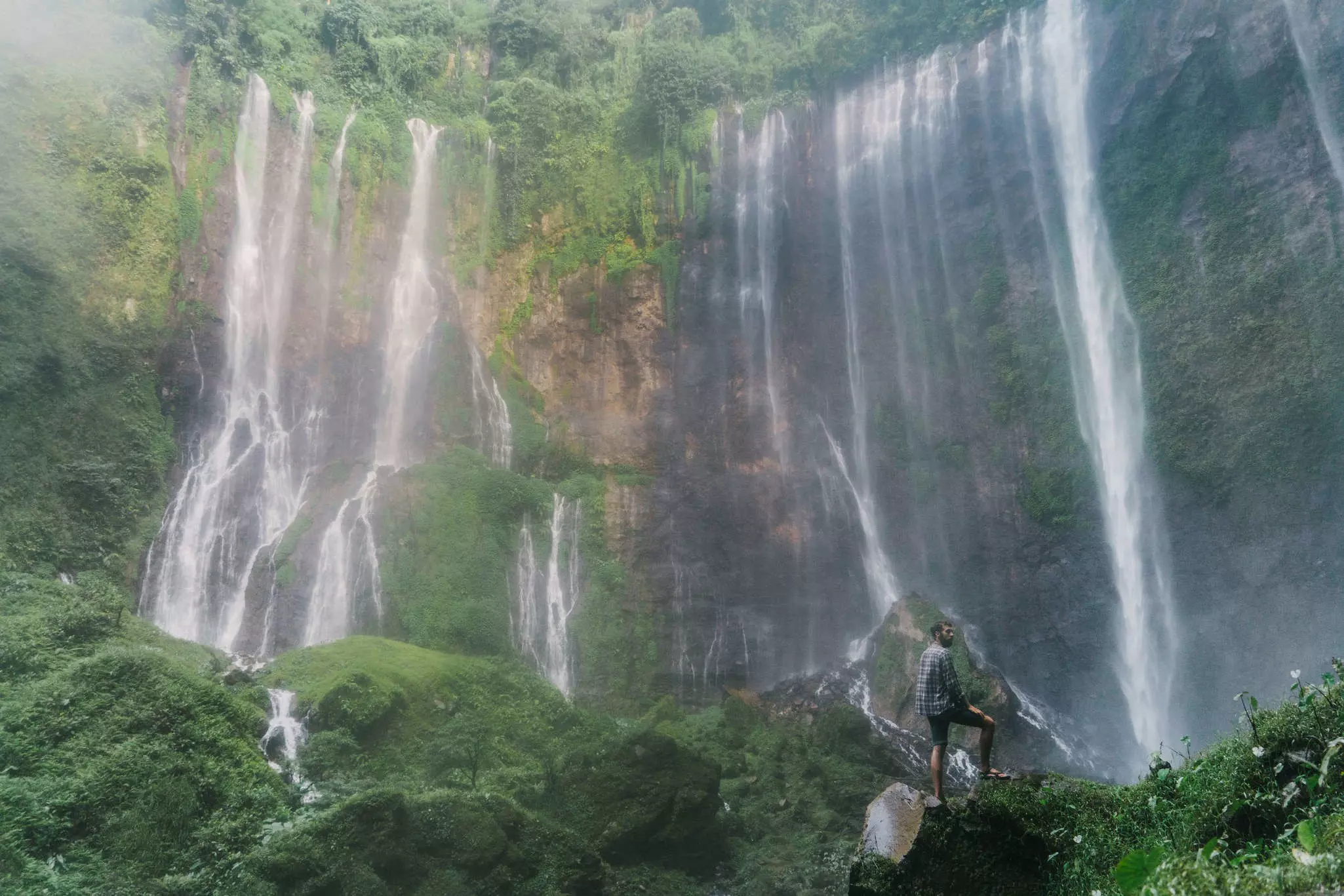 Man standing and looking at Tumpak Sewu waterfall on Java, Indonesia.