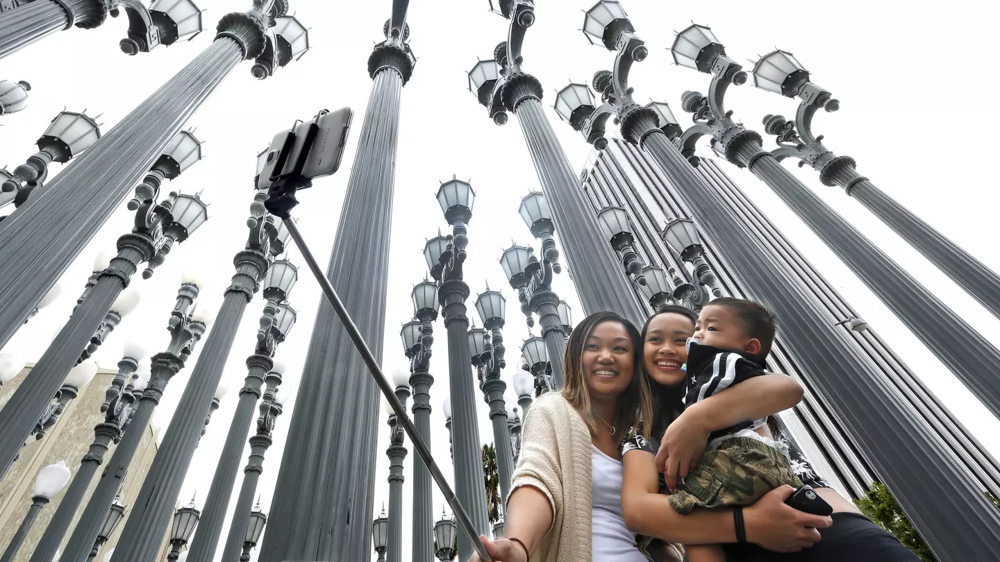 Three people taking a selfie in front of the Urban Light installation at the Los Angeles County Museum of Art