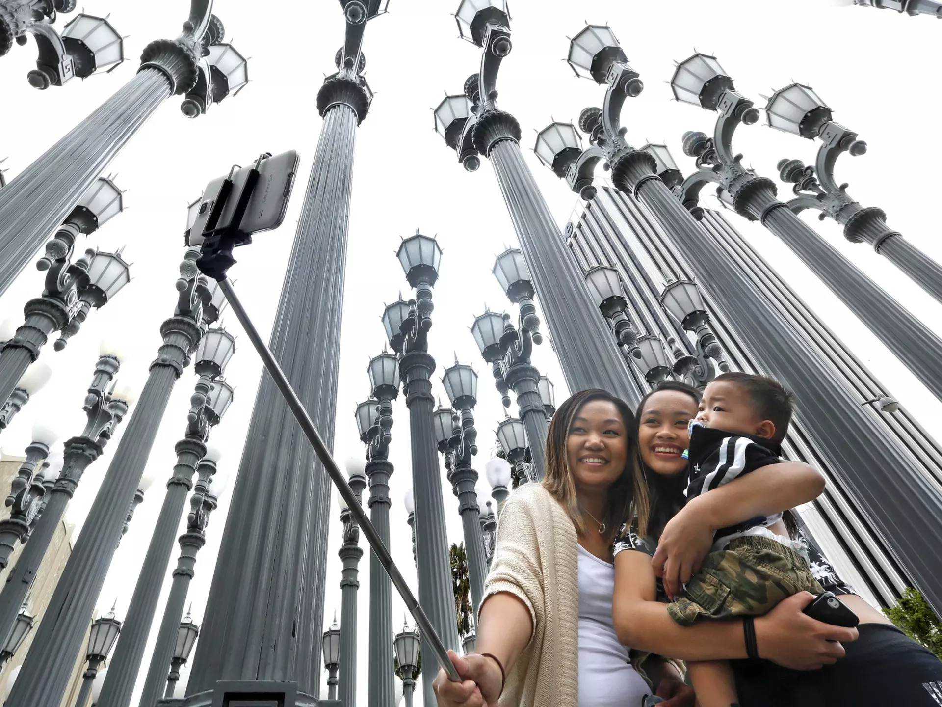Three people taking a selfie in front of the Urban Light installation at the Los Angeles County Museum of Art