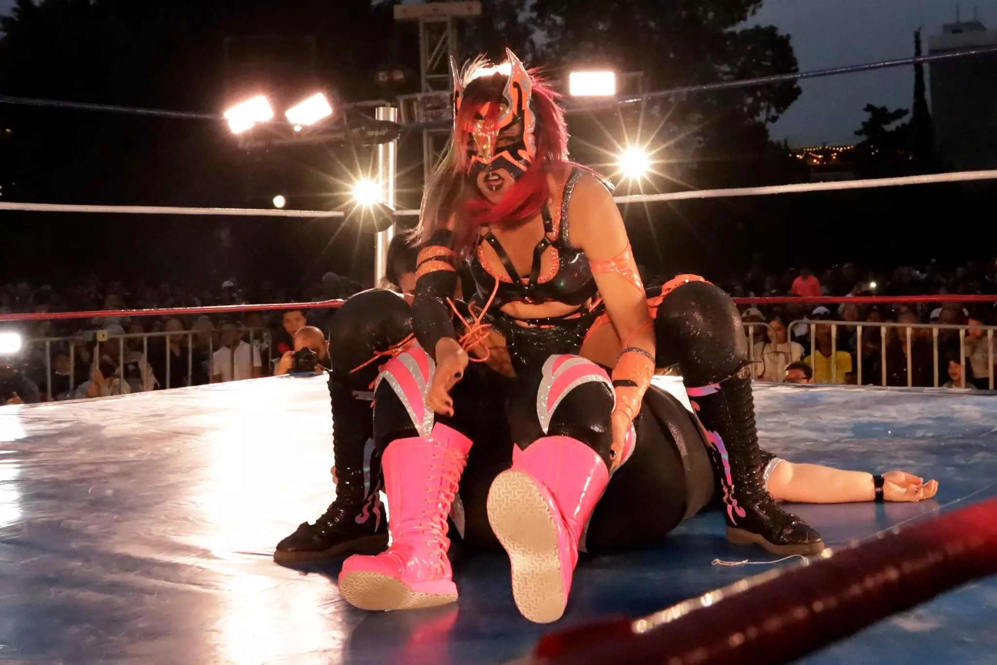 Two women wrestlers in black and pink have a bout on a blue mat under bright lights