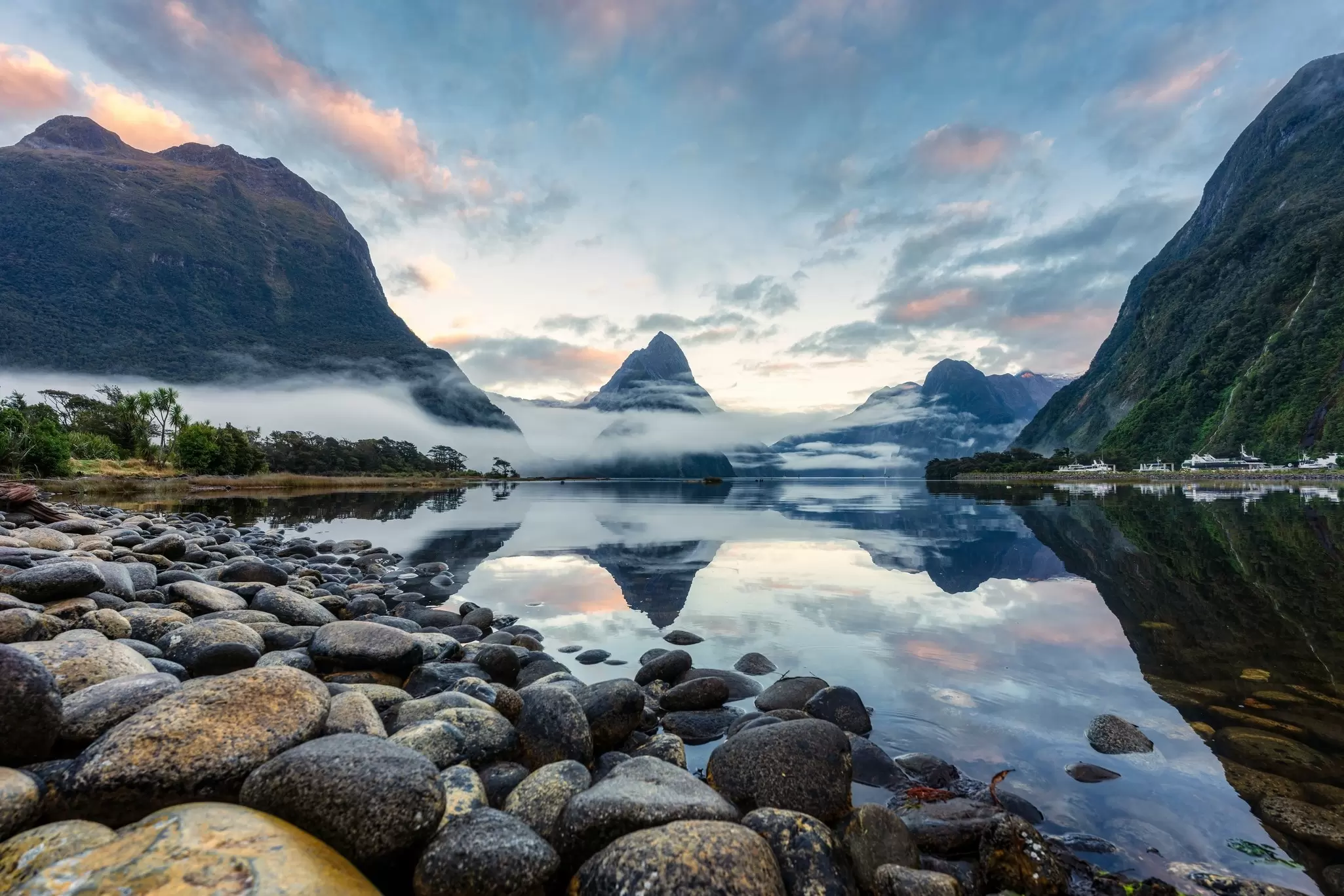 A calm like with a mirrorlike surface reflects clouds and rocky peaks.