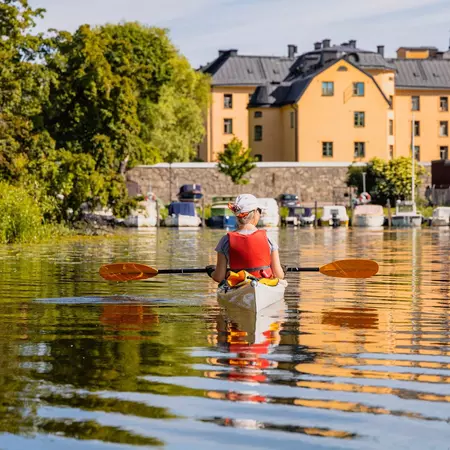 A kayaker on calm waters, with a yellow building in the background.