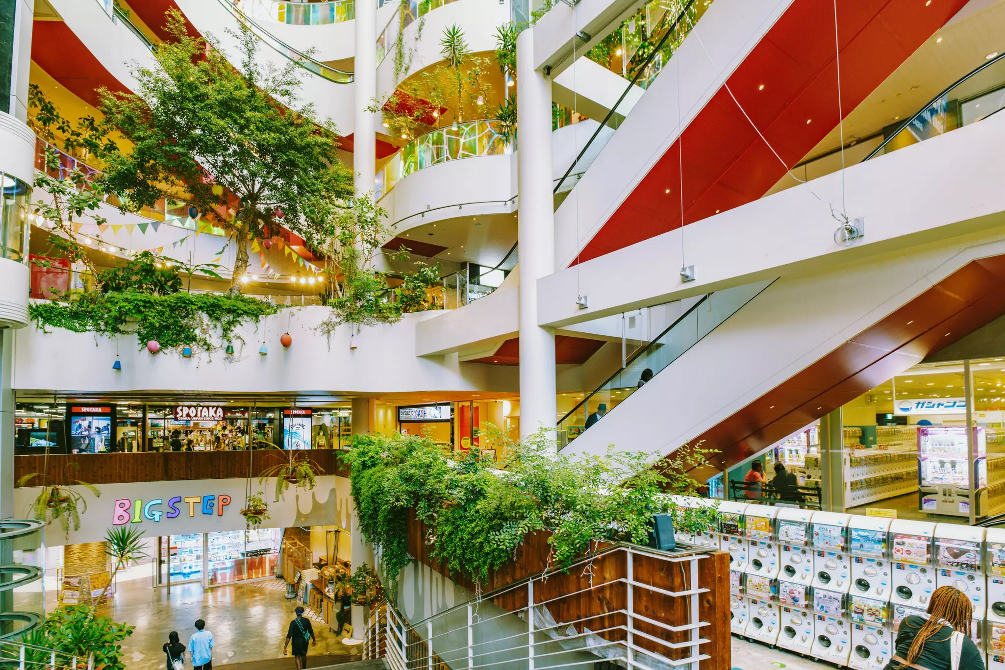 The interior of a shopping mall with open balconies over a central atrium with plants and indoor trees.