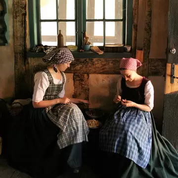 Two girls sewing in traditional clothes at Den Gamle By in Aarhus, Denmark.