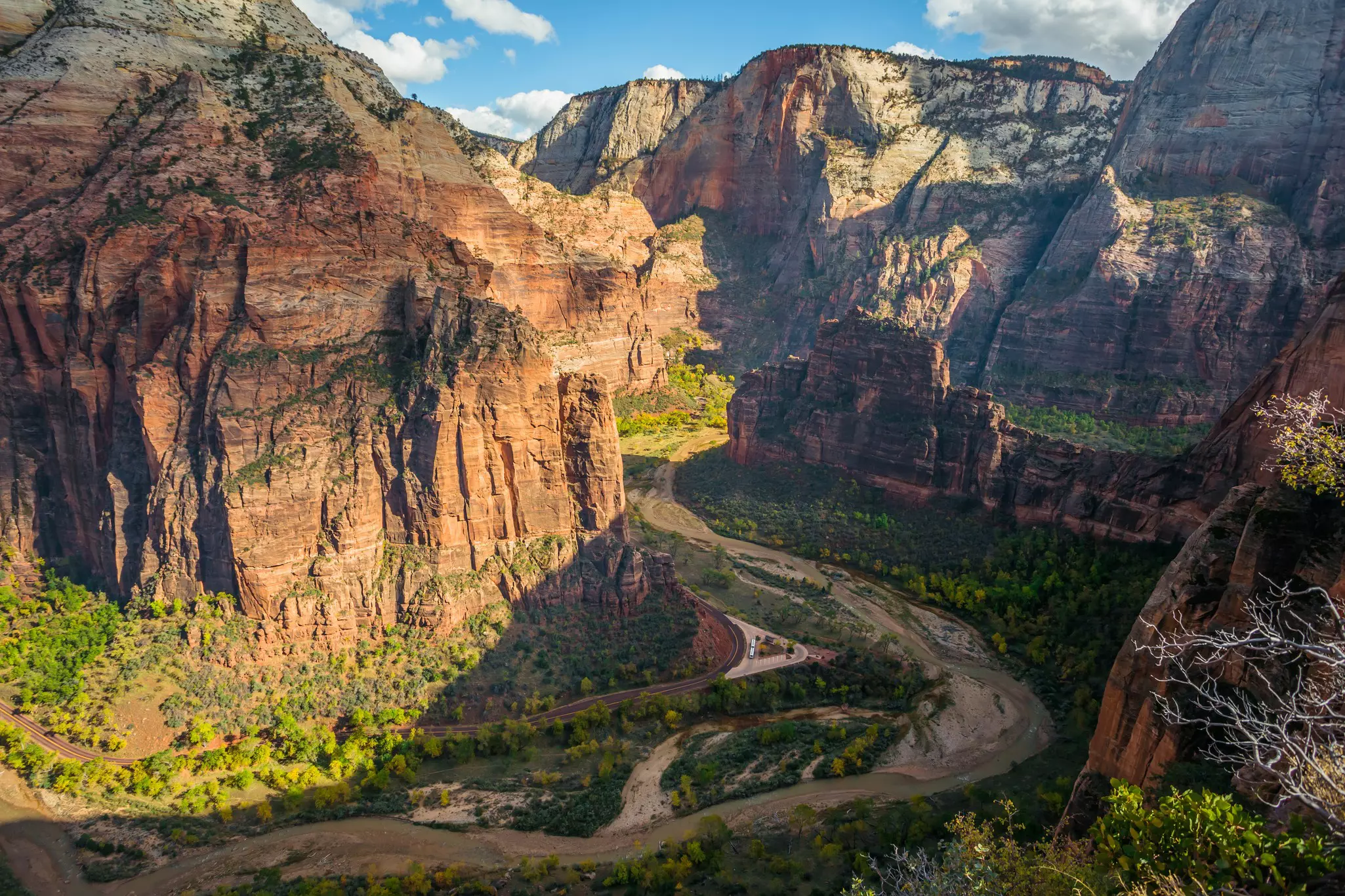 Colorful, rocky valley with river and wavy roads, green forest and blue sky with clouds, photographed from cliff.