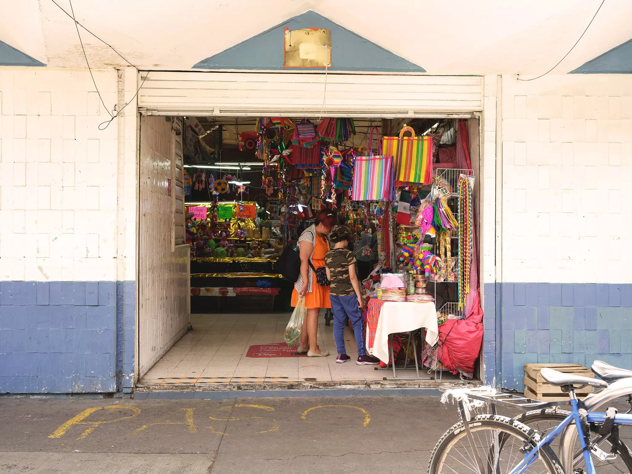 Two shoppers stand in the entryway of a market, looking at colorful bags, pinatas and more