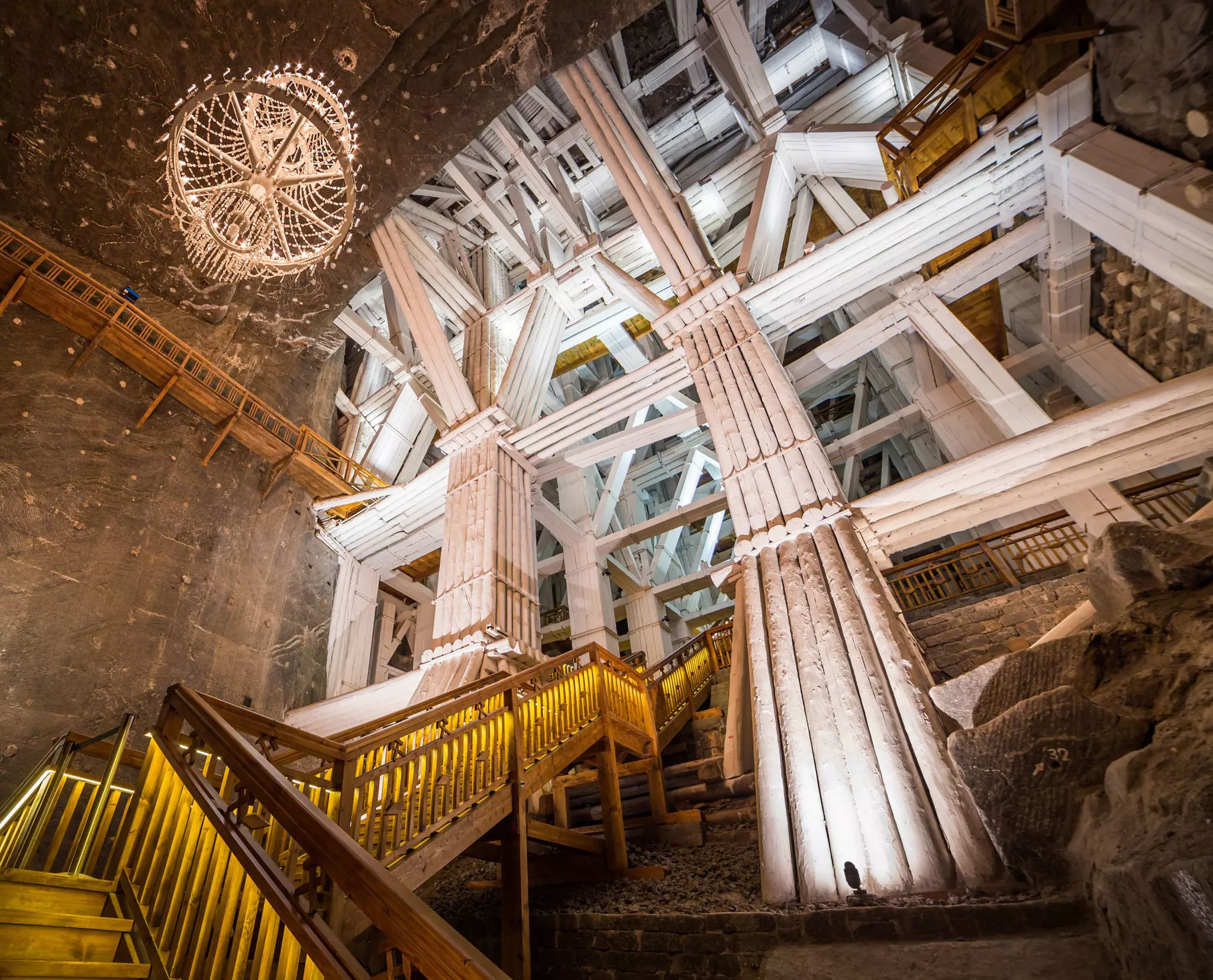 A staircase inside a salt mine in Poland; a large chandelier hangs from the vaulted ceiling.