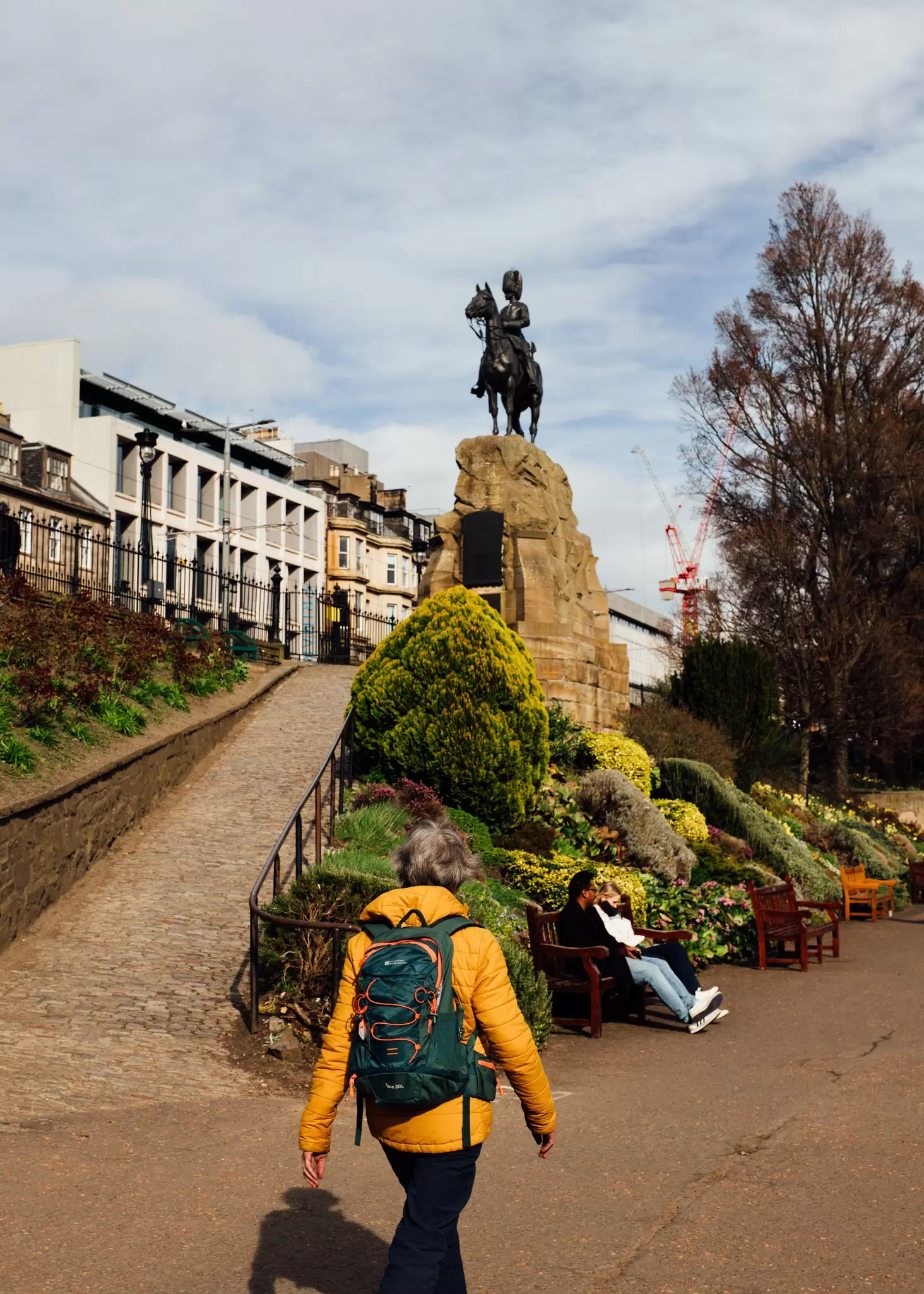 A person in a yellow jacket wearing a backpack walks on a path in park
