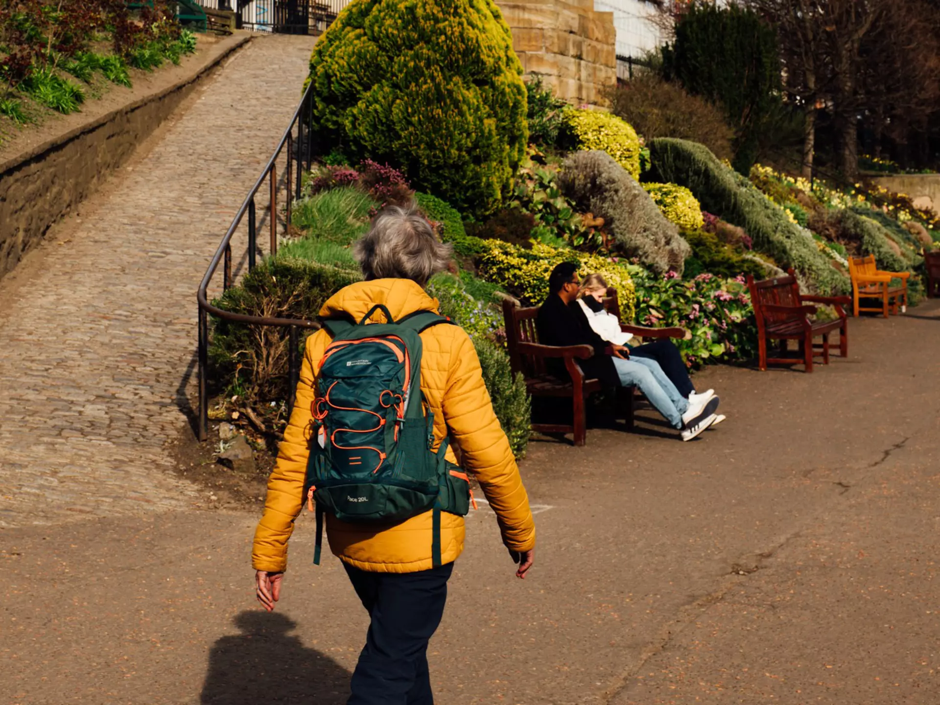 A person in a yellow jacket wearing a backpack walks on a path in park
