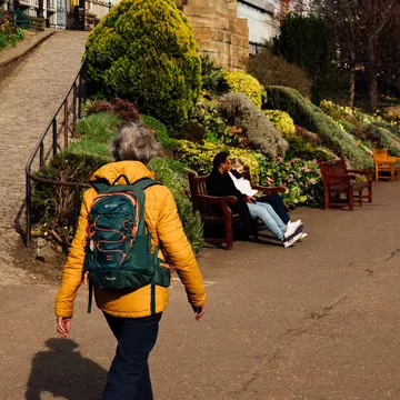 A person in a yellow jacket wearing a backpack walks on a path in park