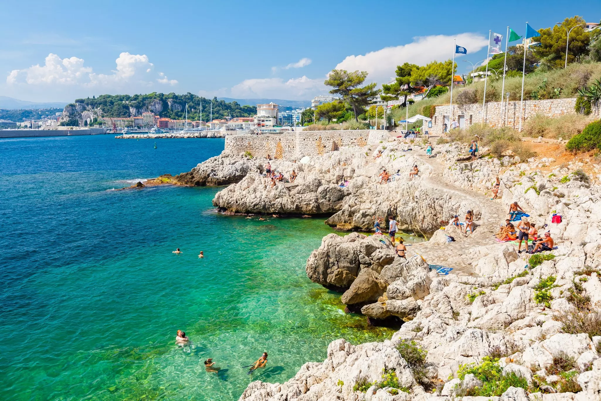 People cluster in swimsuits on rocks leading to the sea before taking a swim