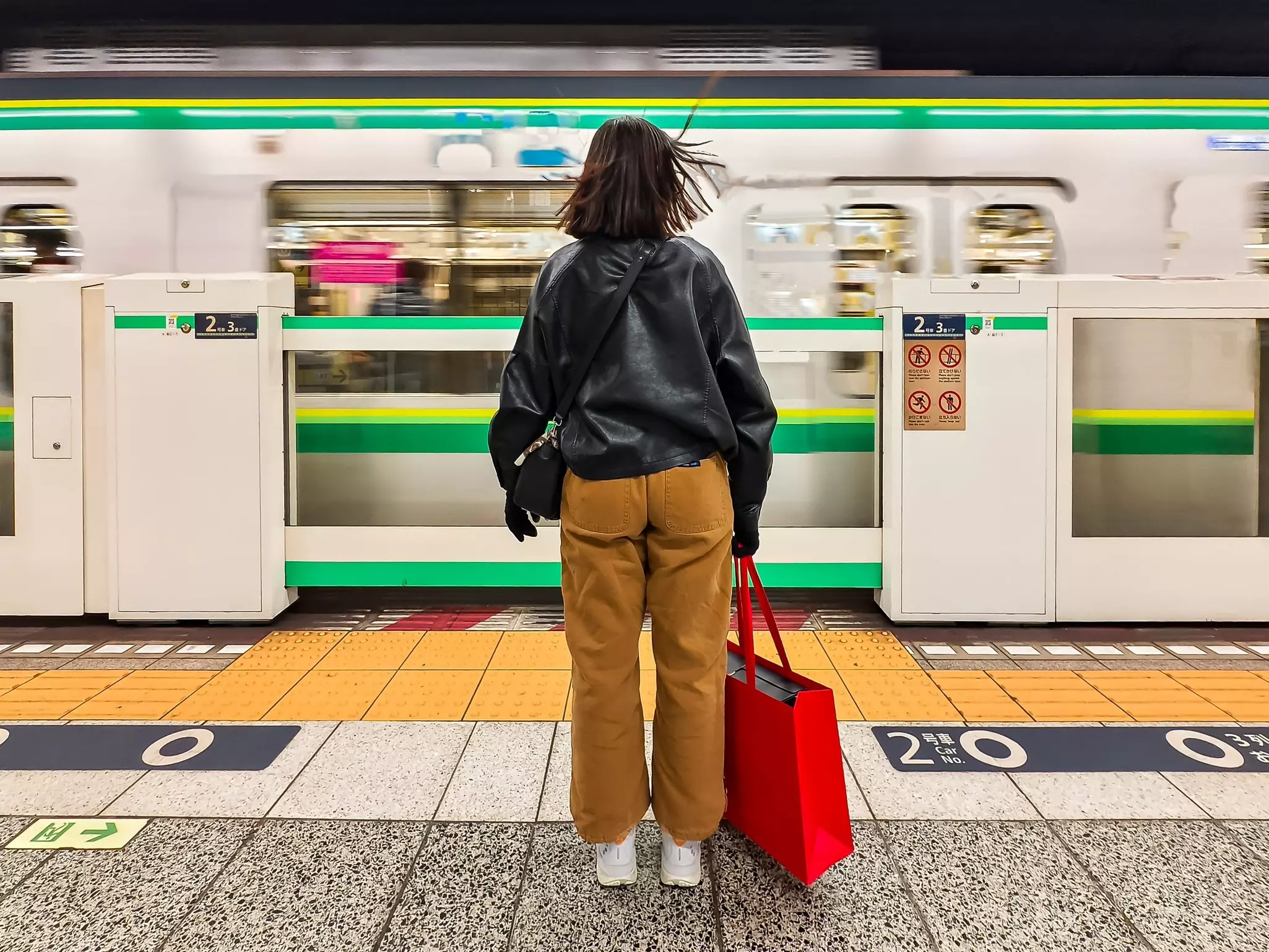 Young woman with red shopping bag waiting as train passes at Hibiya subway station