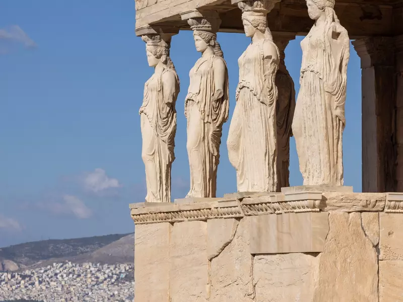 Four columns sculpted to look like women hold up an ancient ruin in Greece. 