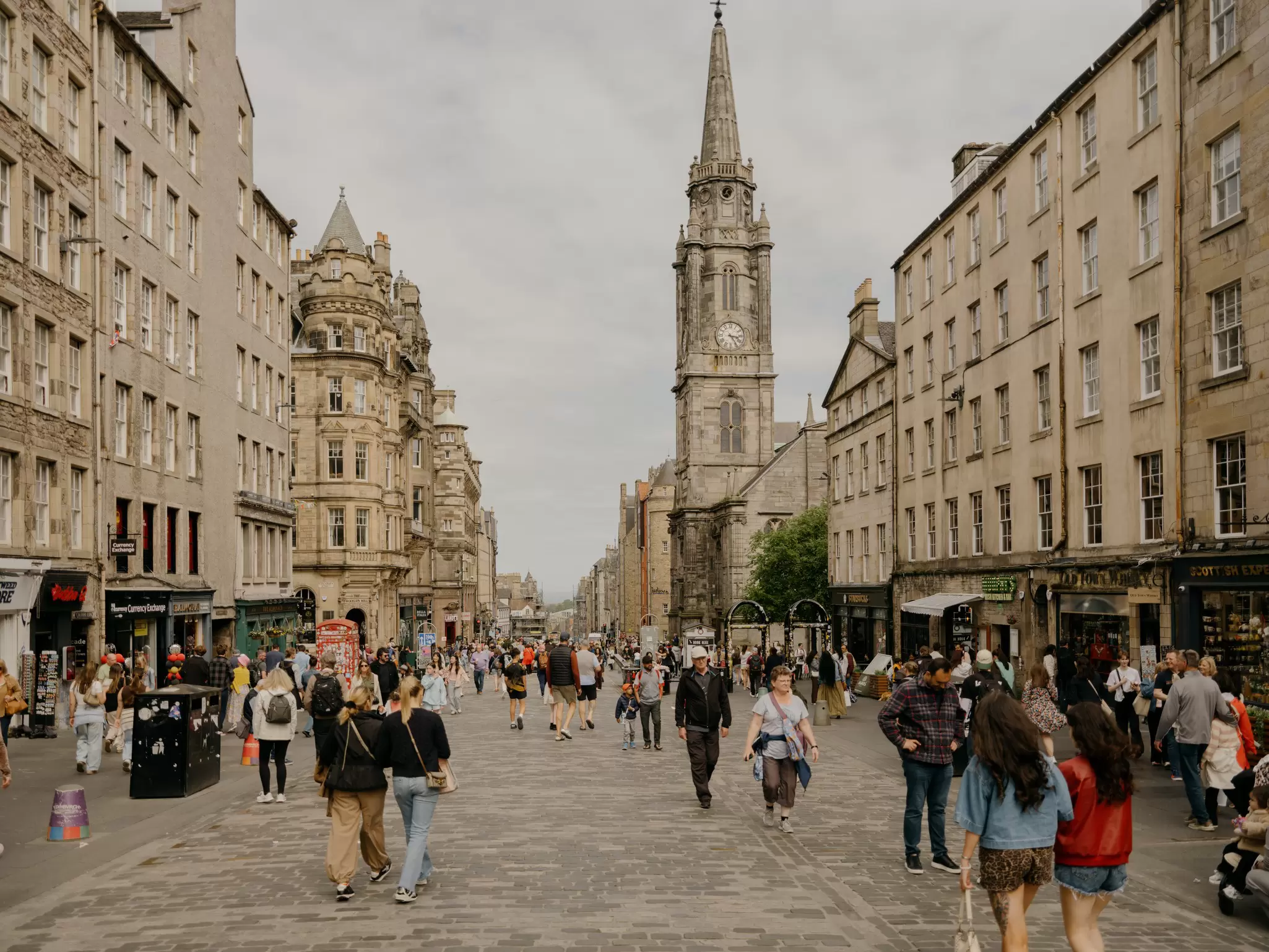 People walking along a cobbled street lined with Victorian buildings and a tall church steeple