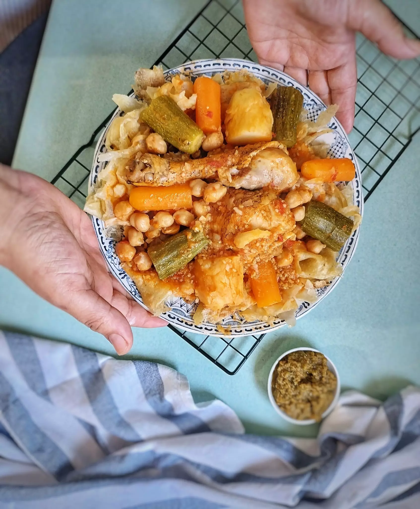 Hands hold out a bowl of chickpeas, vegetables and chicken on top of shredded flatbread.