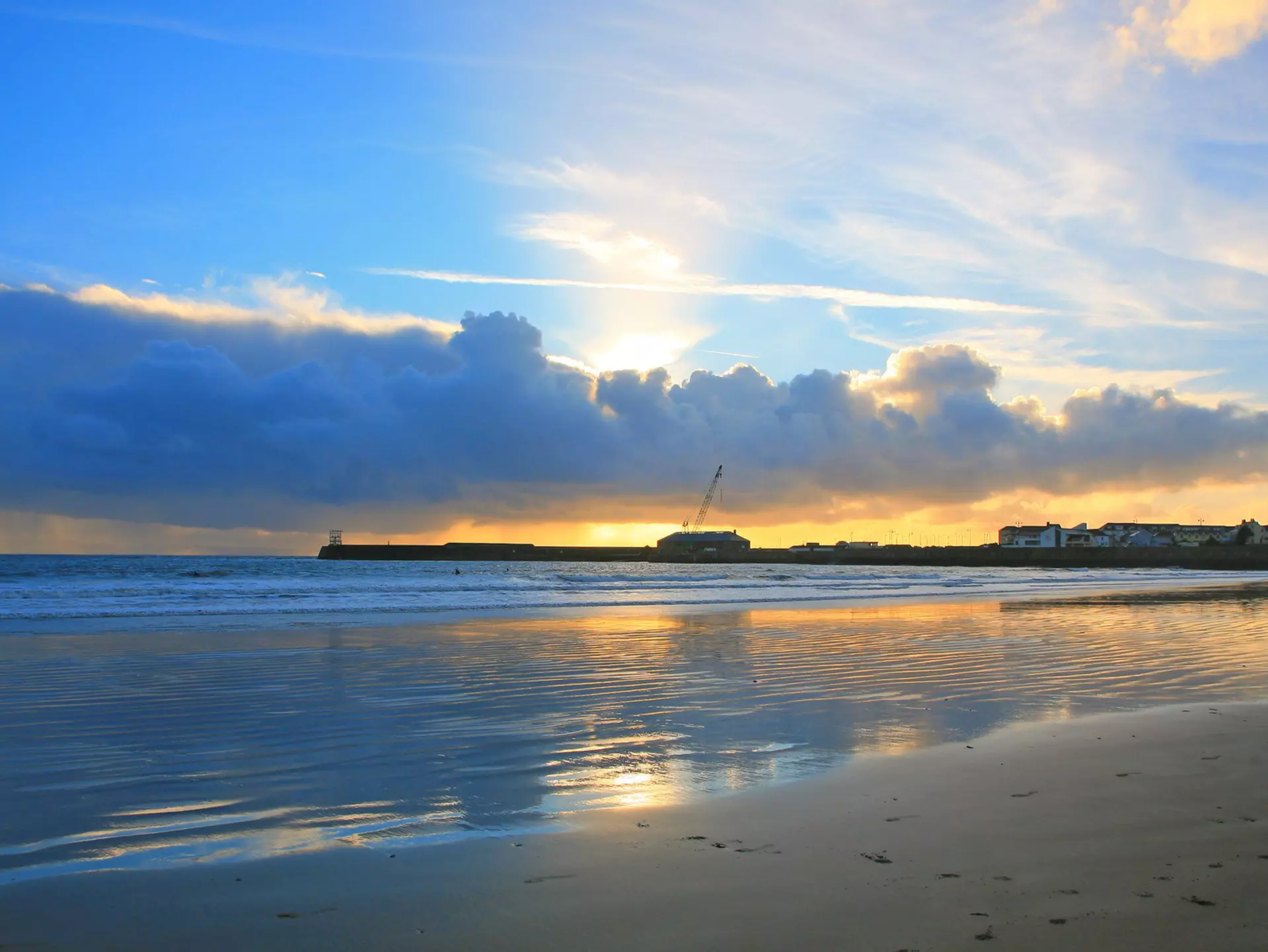 Sunset over beach reflecting in the wet sand with headland in the distance.