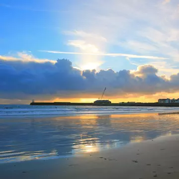 Sunset over beach reflecting in the wet sand with headland in the distance.