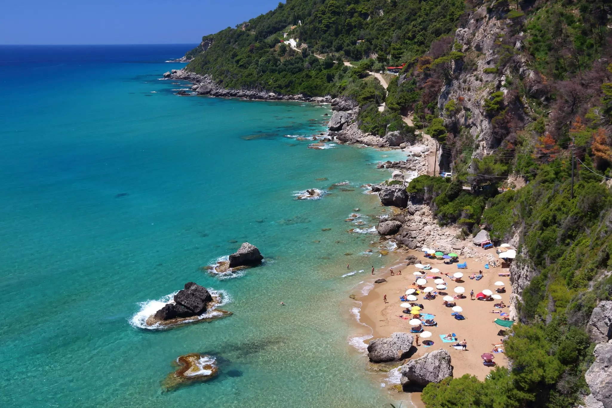 Aerial shot of a beach near cliffs and dotted with sun umbrellas
