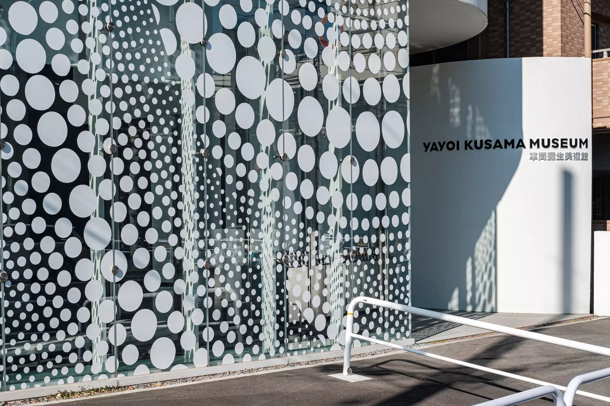 The entrance to a museum in Tokyo, with a glass wall patterned with polka dots casting a shadow.