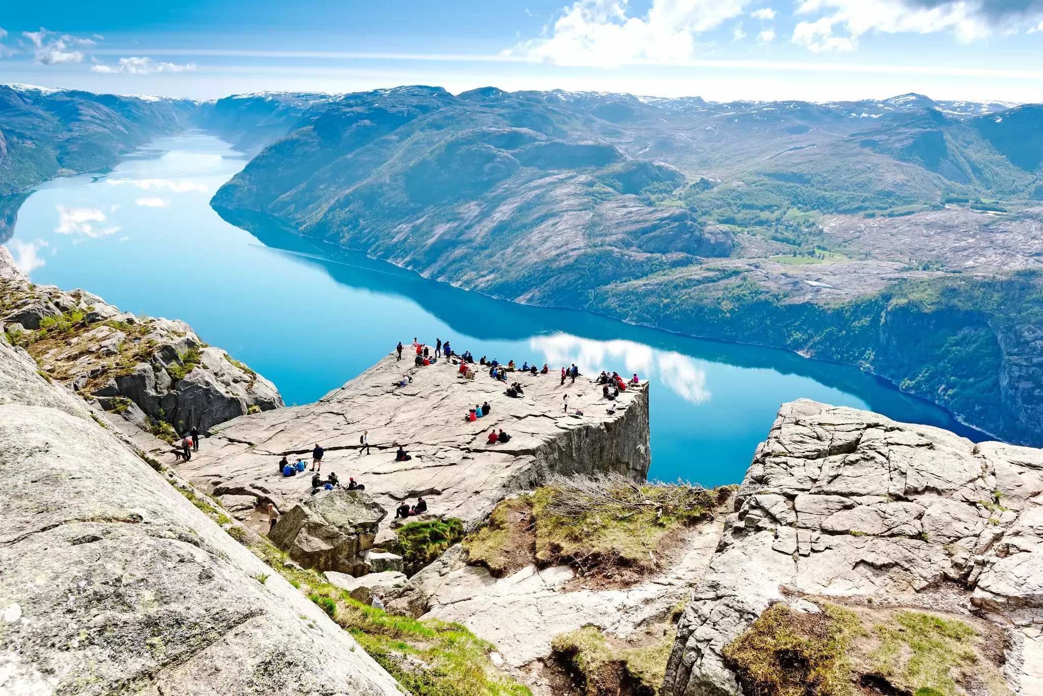 Travelers stand on the dramatic Preikestolen outcrop overlooking Lysefjord near Stavanger in Norway. 