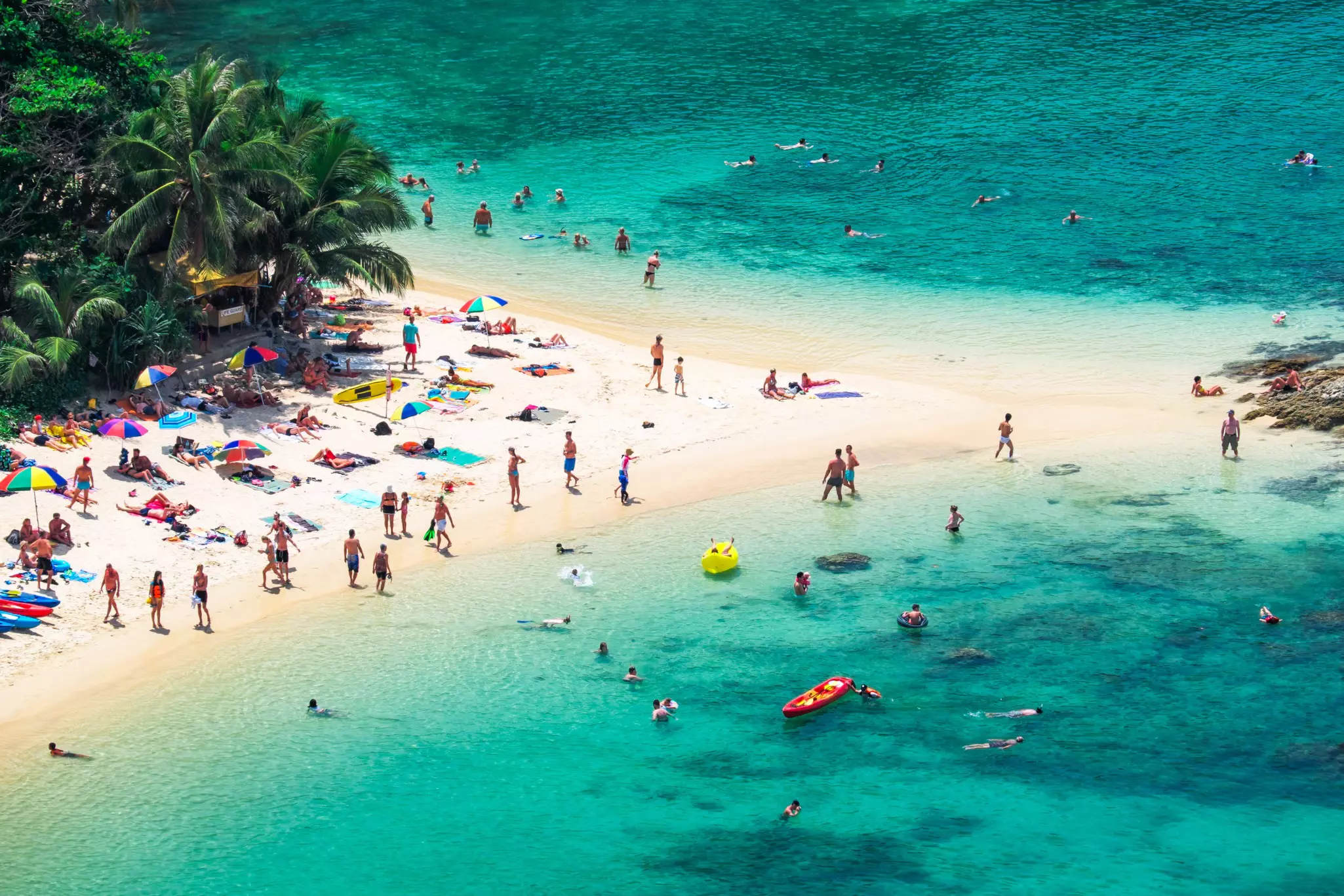 An aerial view of people on a beach and in the water of a sandbank on a tropical island.
