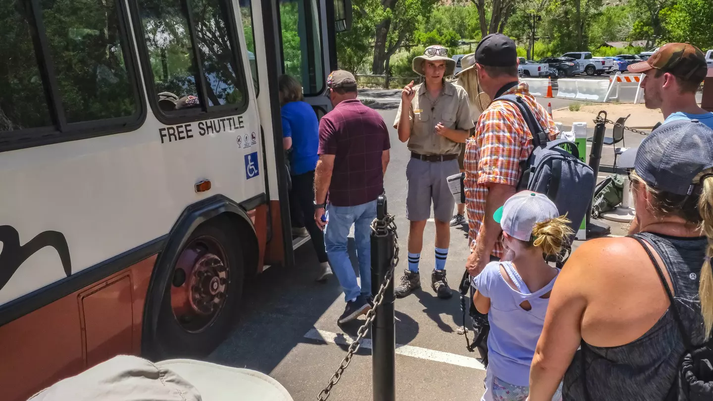 A park ranger stands next to a shuttle bus as people wait to board at Zion National Park.