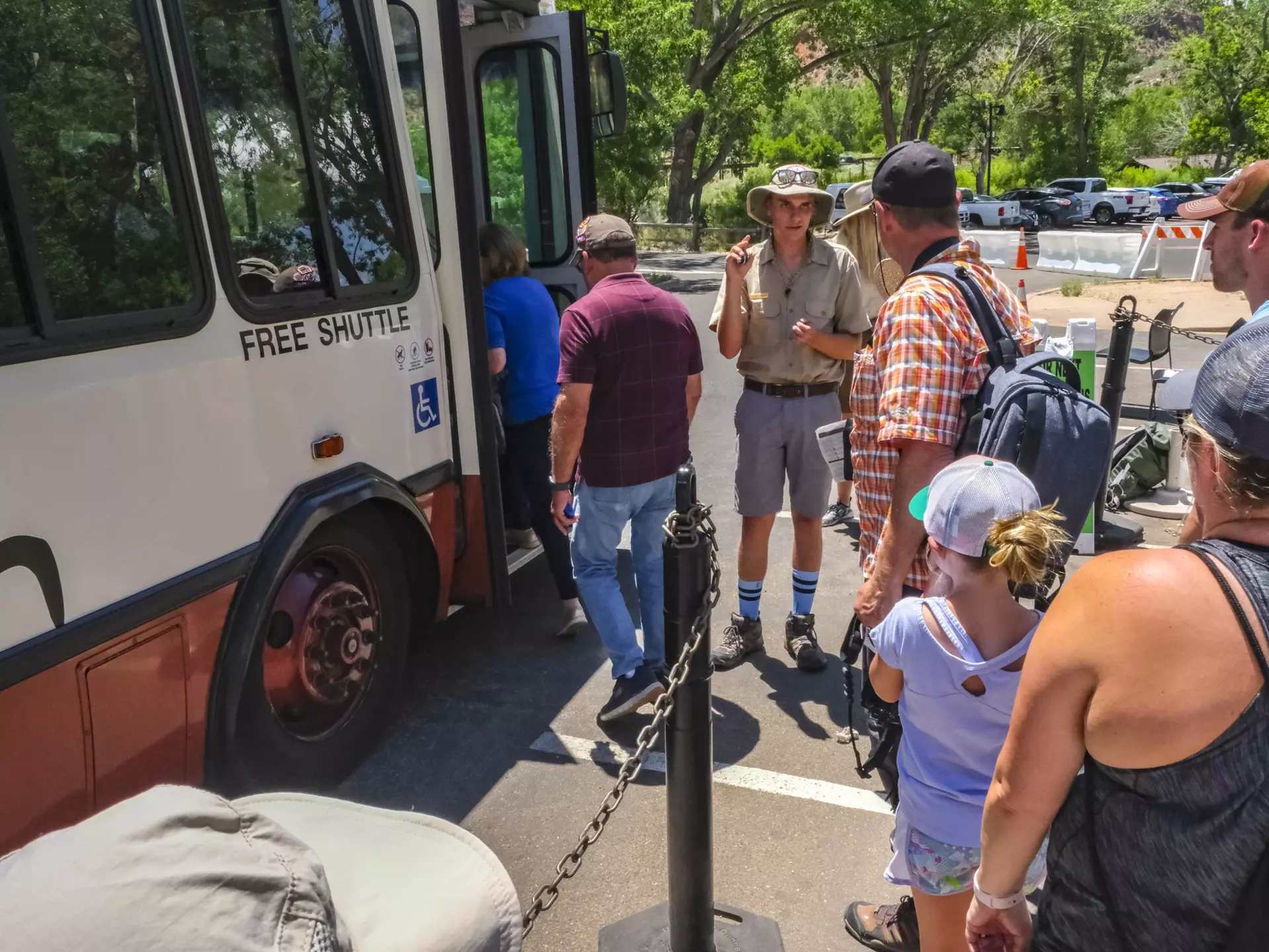 A park ranger stands next to a shuttle bus as people wait to board at Zion National Park.