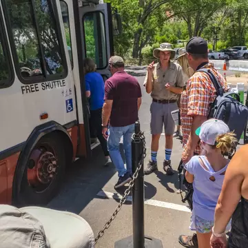 A park ranger stands next to a shuttle bus as people wait to board at Zion National Park.