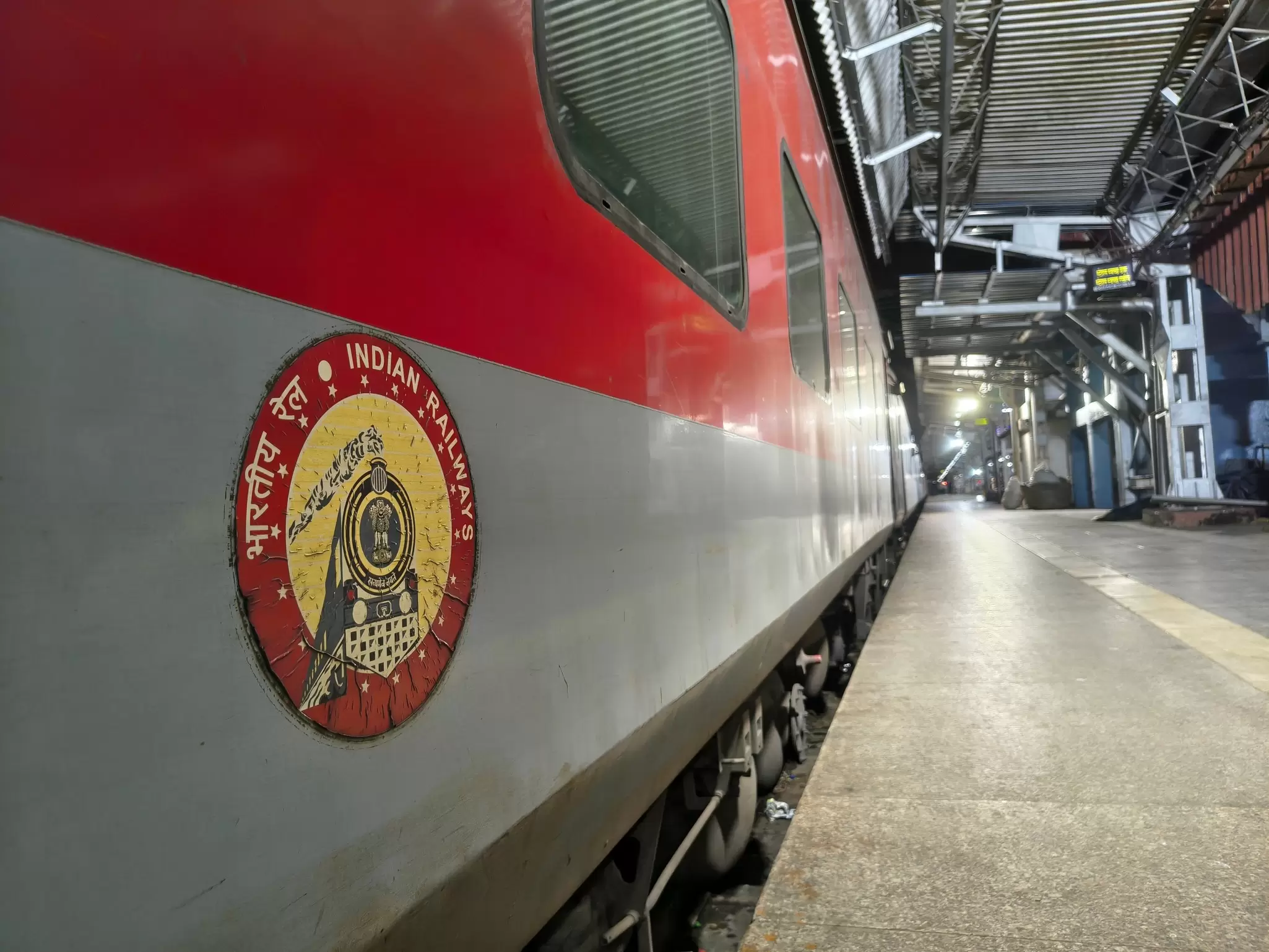 A train on the platform in Mumbai, India, with the Indian Railways logo in the foreground. 