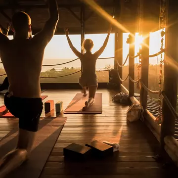 People practice yoga in an open yoga studio near the ocean in Costa Rica while the sun sets..