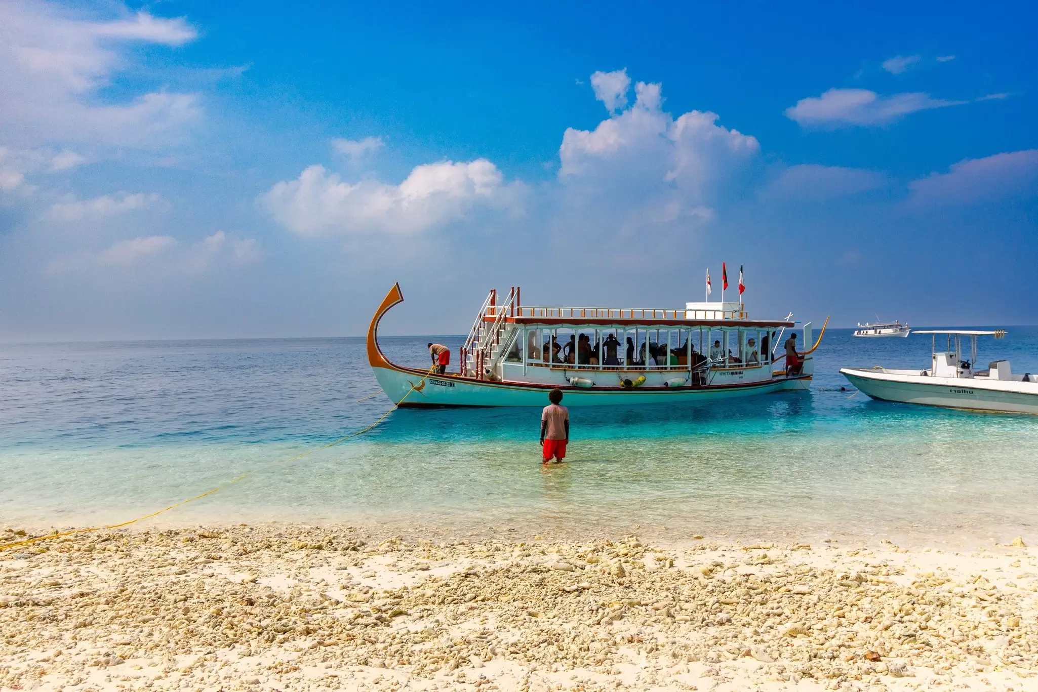 A man stands in the shallows of the ocean near the edge of a sandy beach to direct a tour boat in Fulidhoo, Maldives