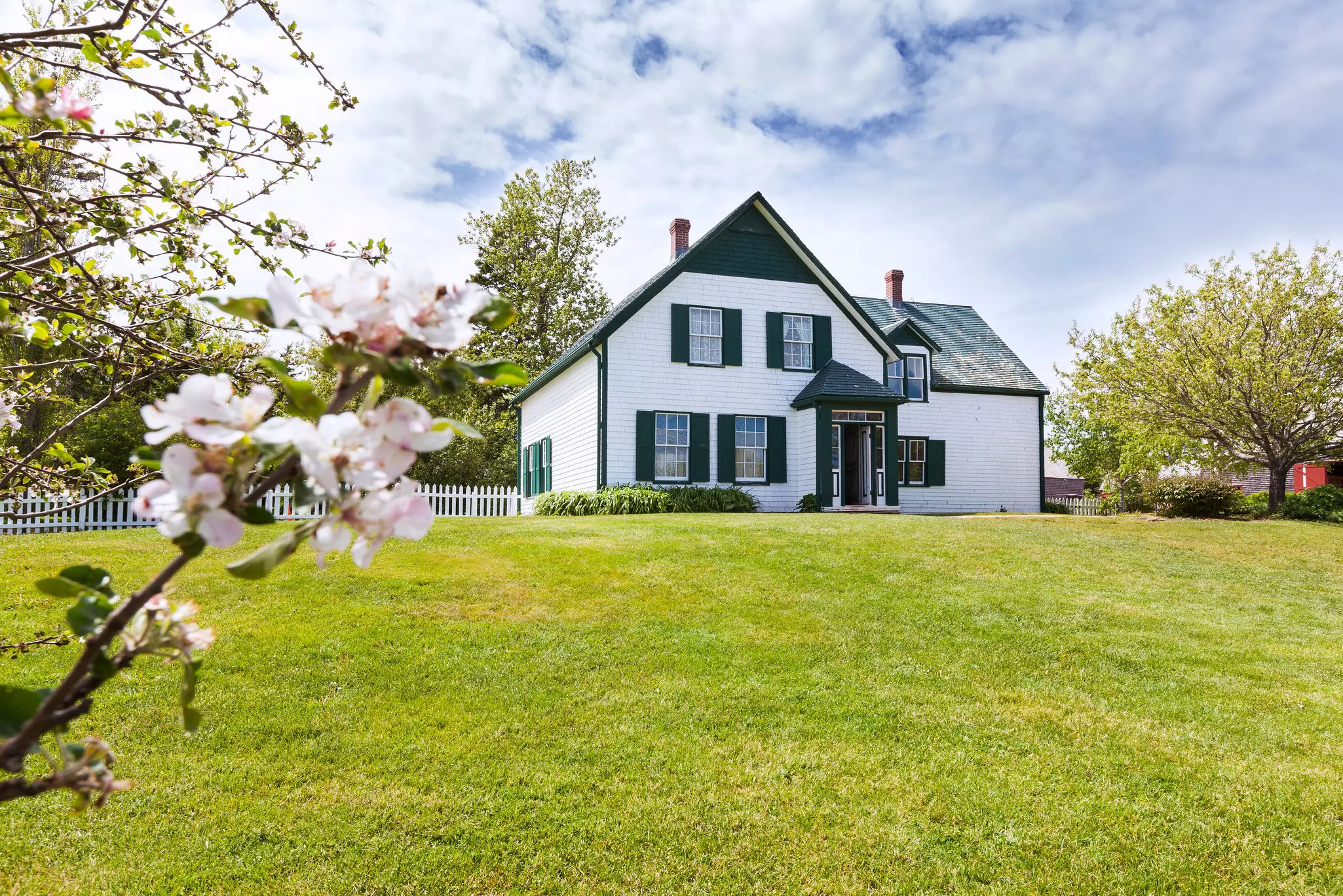 A gorgeous house with shuttered windows and a green gabled roof among large lawns in spring.