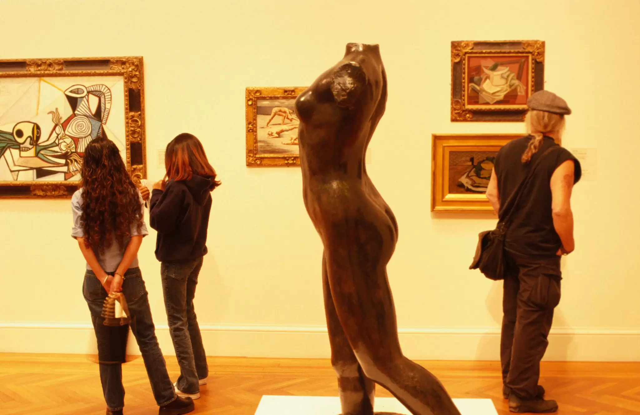 A small group of visitors nose around one of the rooms in the Legion of Honor in San Francisco. Paintings hang on the wall and a sculpture takes up much of the foreground.