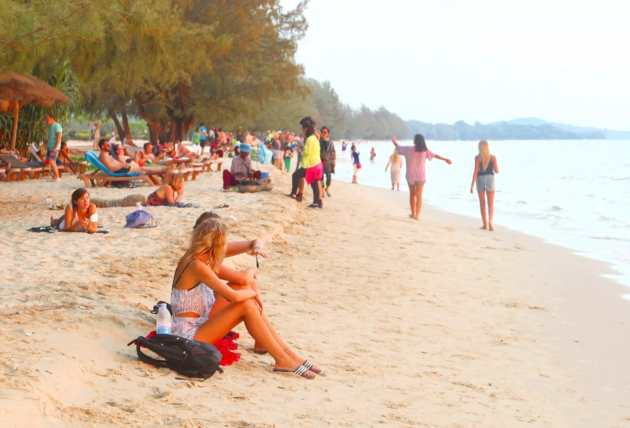 People sitting, lounging and walking on a white sand beach in Cambodia.