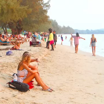 People sitting, lounging and walking on a white sand beach in Cambodia.