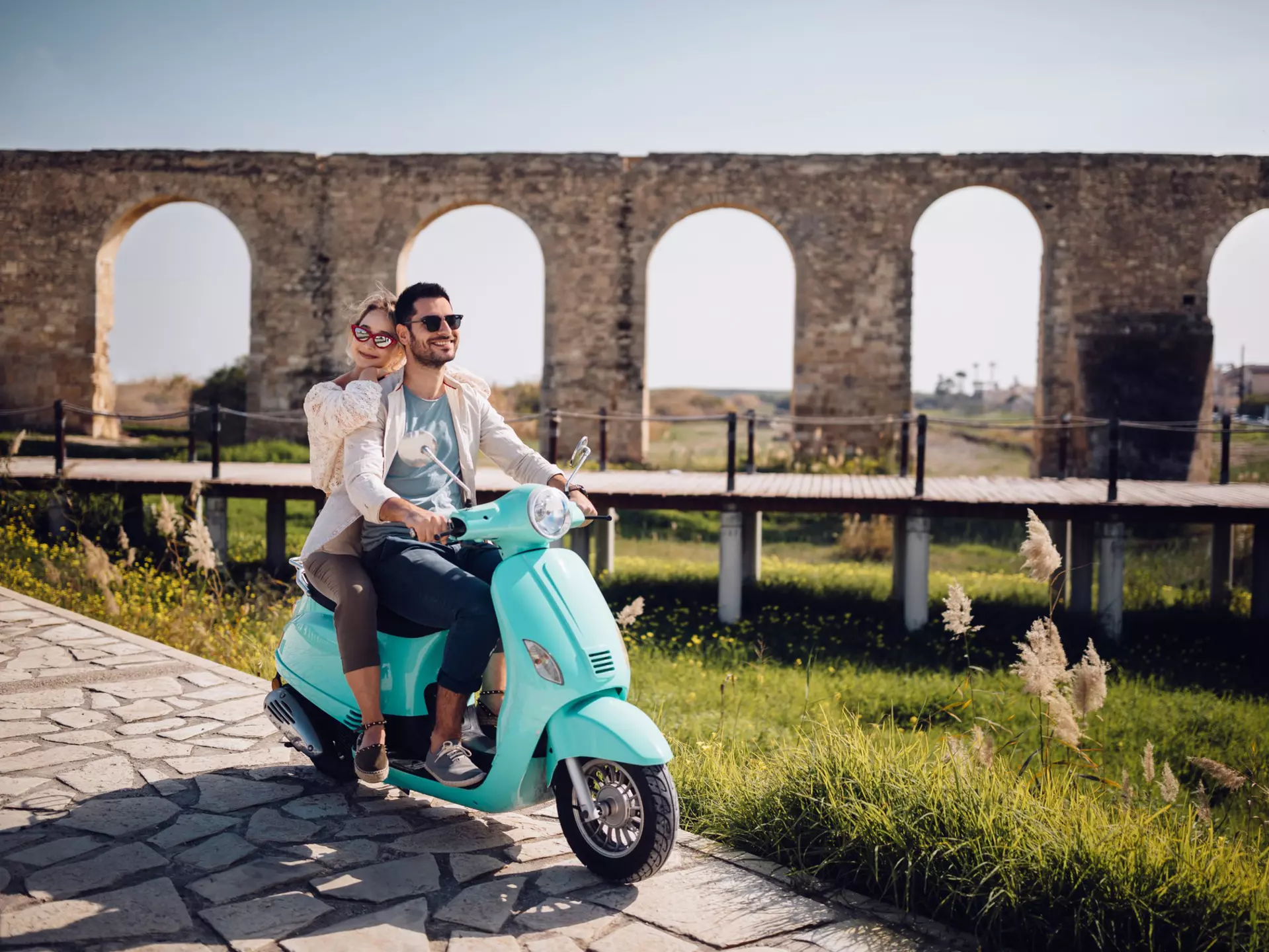 Young loving couple with vintage motorcycle riding next to ancient stone aqueduct monument in Cyprus
967273278