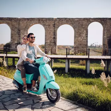Young loving couple with vintage motorcycle riding next to ancient stone aqueduct monument in Cyprus
967273278