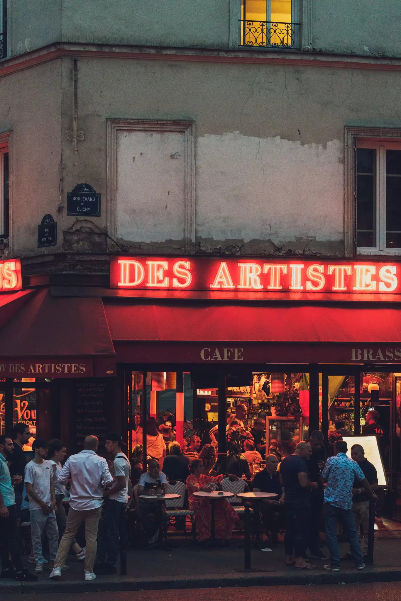 People gather at terrace tables outside a cafe-bar at night.