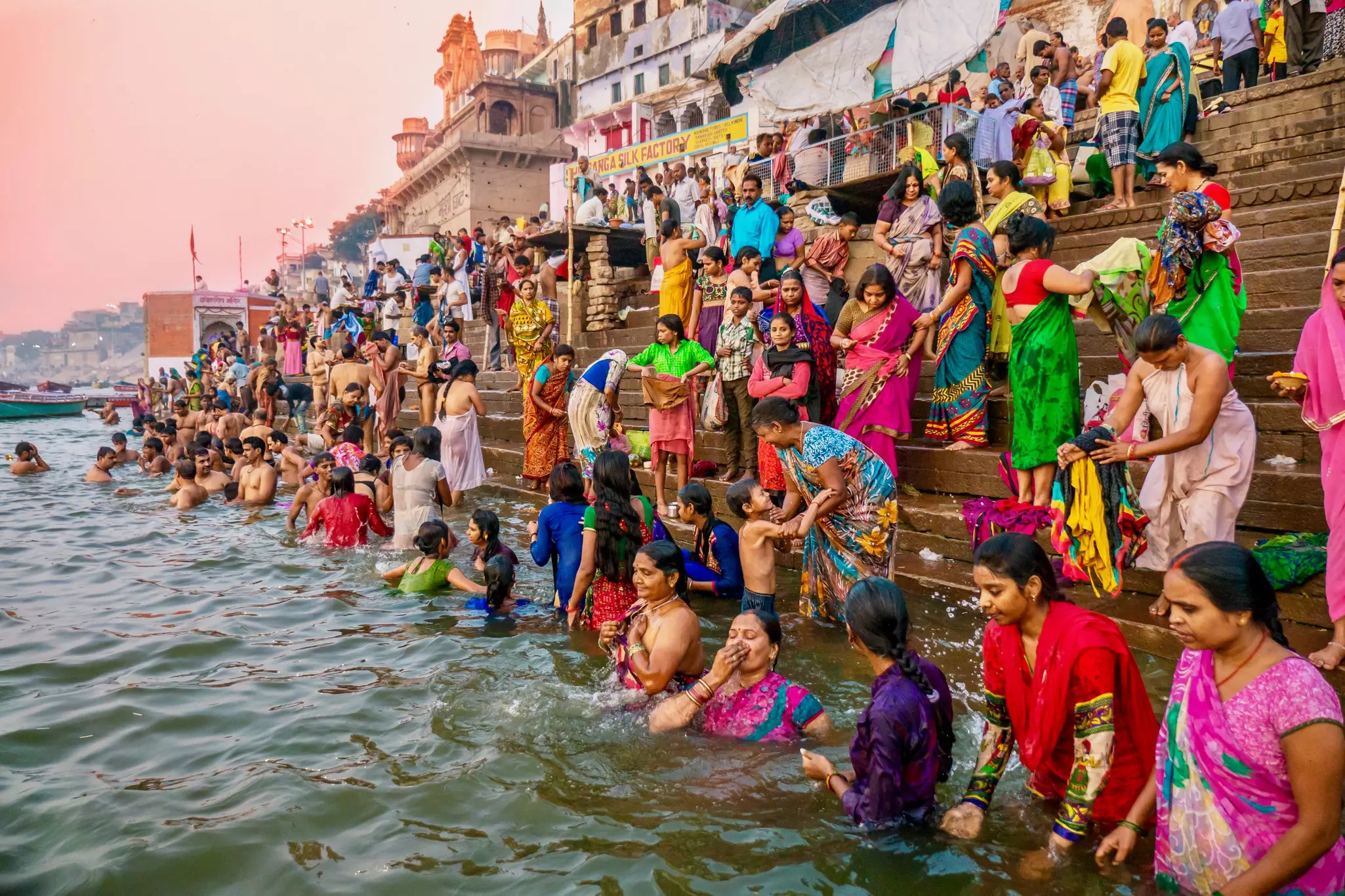 Women in colorful saris descent steps into the water of a river.