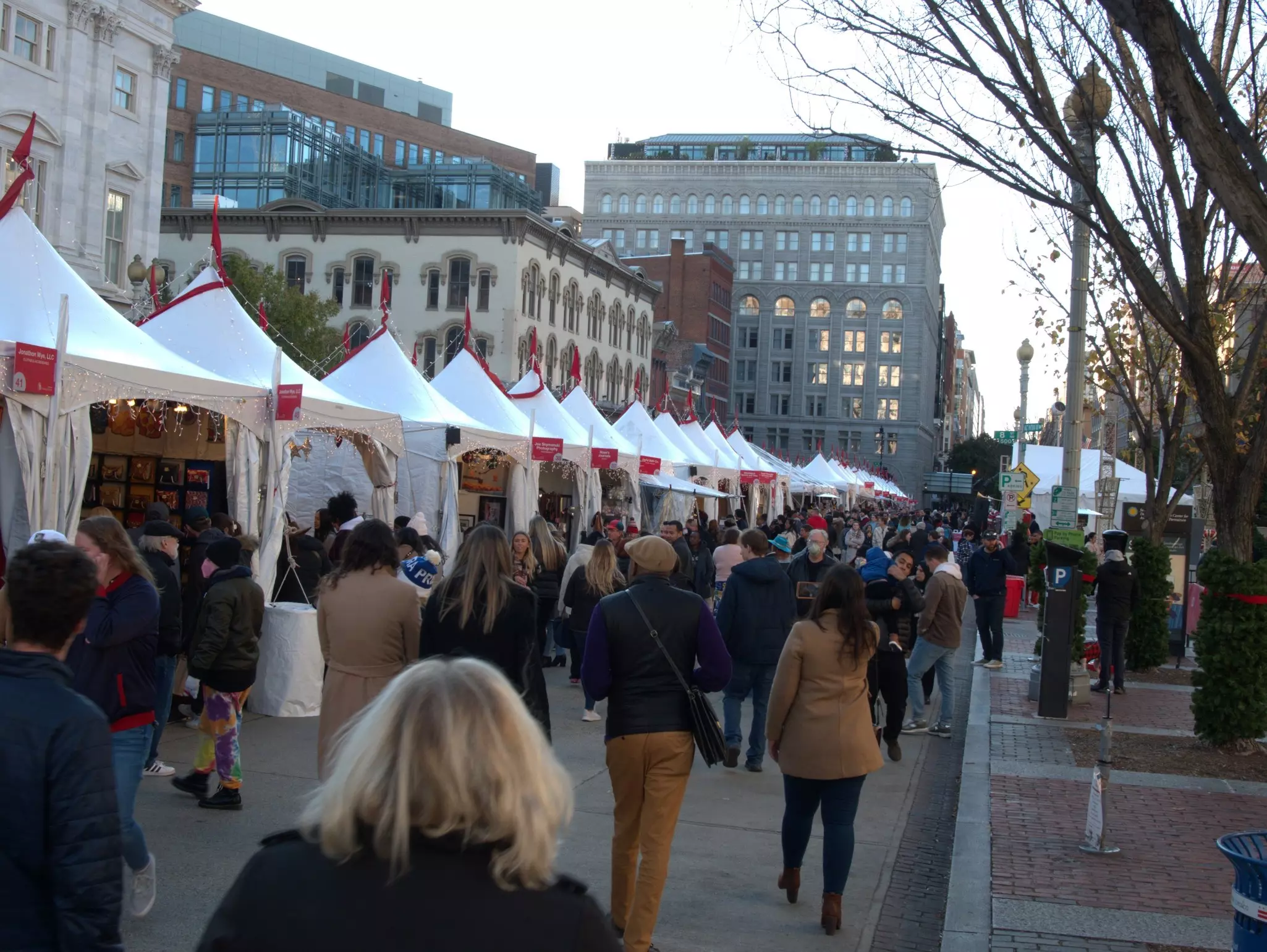 People walking by white-tented booths in a city's open-air market
