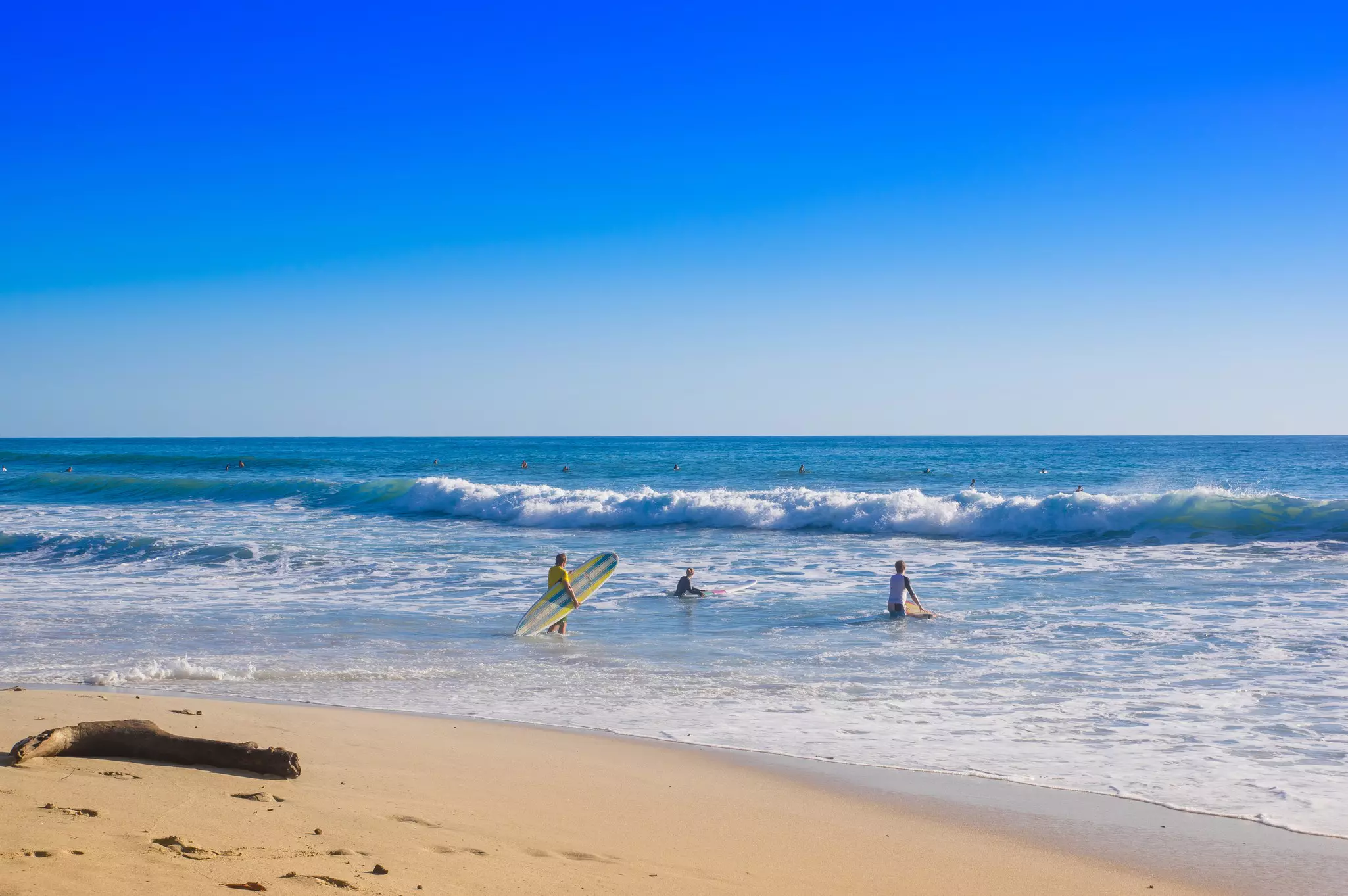Outdoor view of surfers on the beach of Santa Teresa on a beautiful sunny day with blue sky and blue water in Costa Rica.