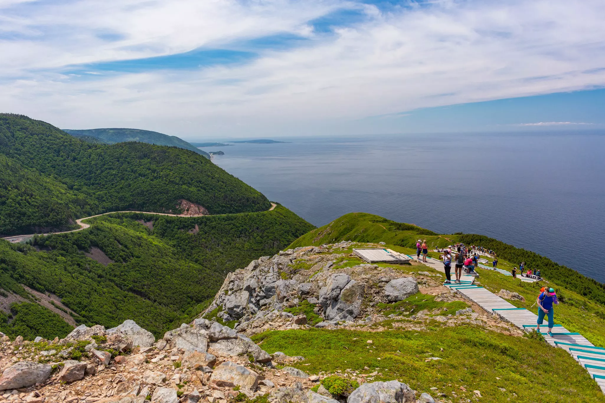 Hikers follow a boardwalk over the top of a cliff with extensive coastal views.