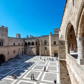A wide view of people standing in the courtyard of a medieval palace in a city.