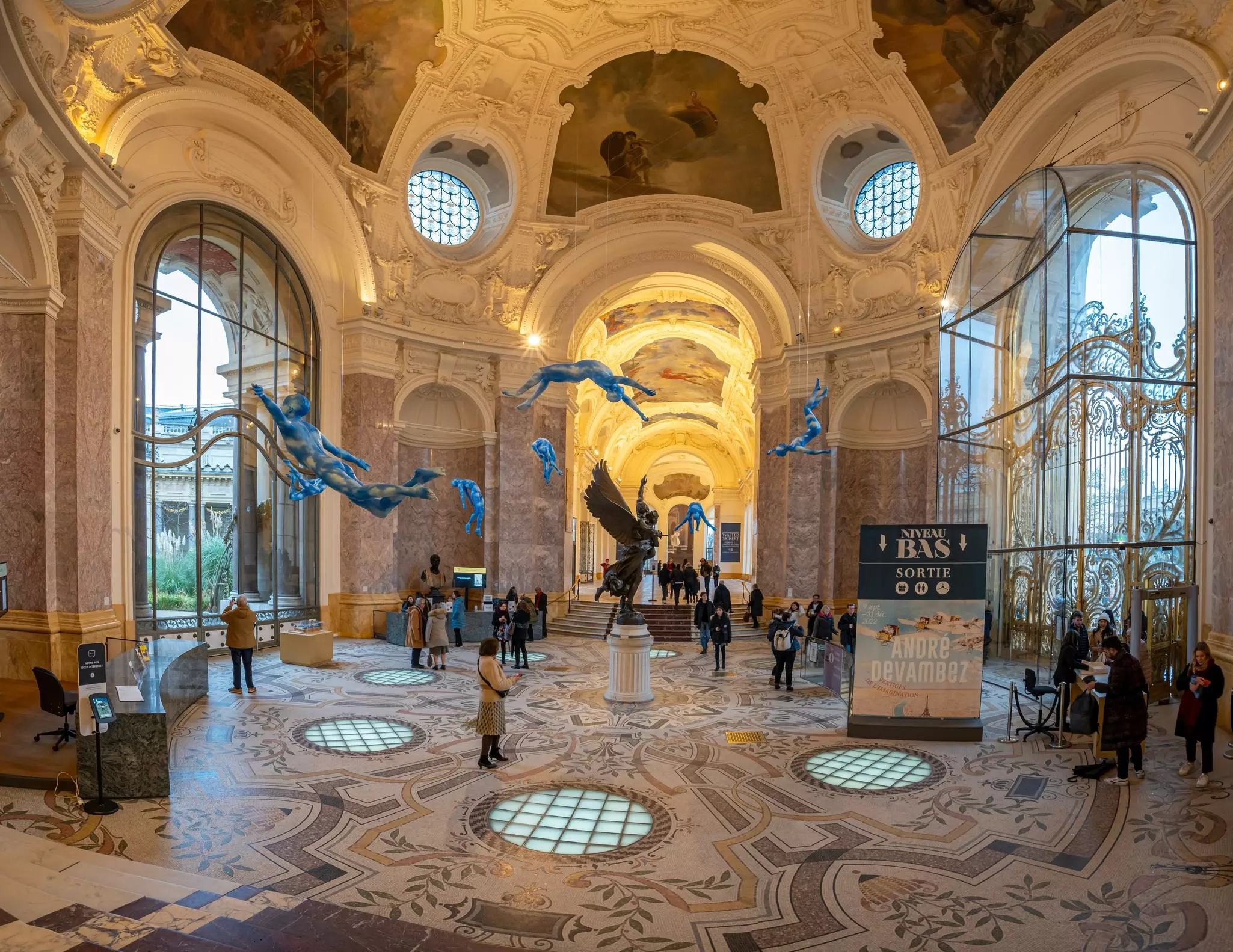 People in the ornate rotunda of a museum, with a patterned floor and items suspended from the ceiling.