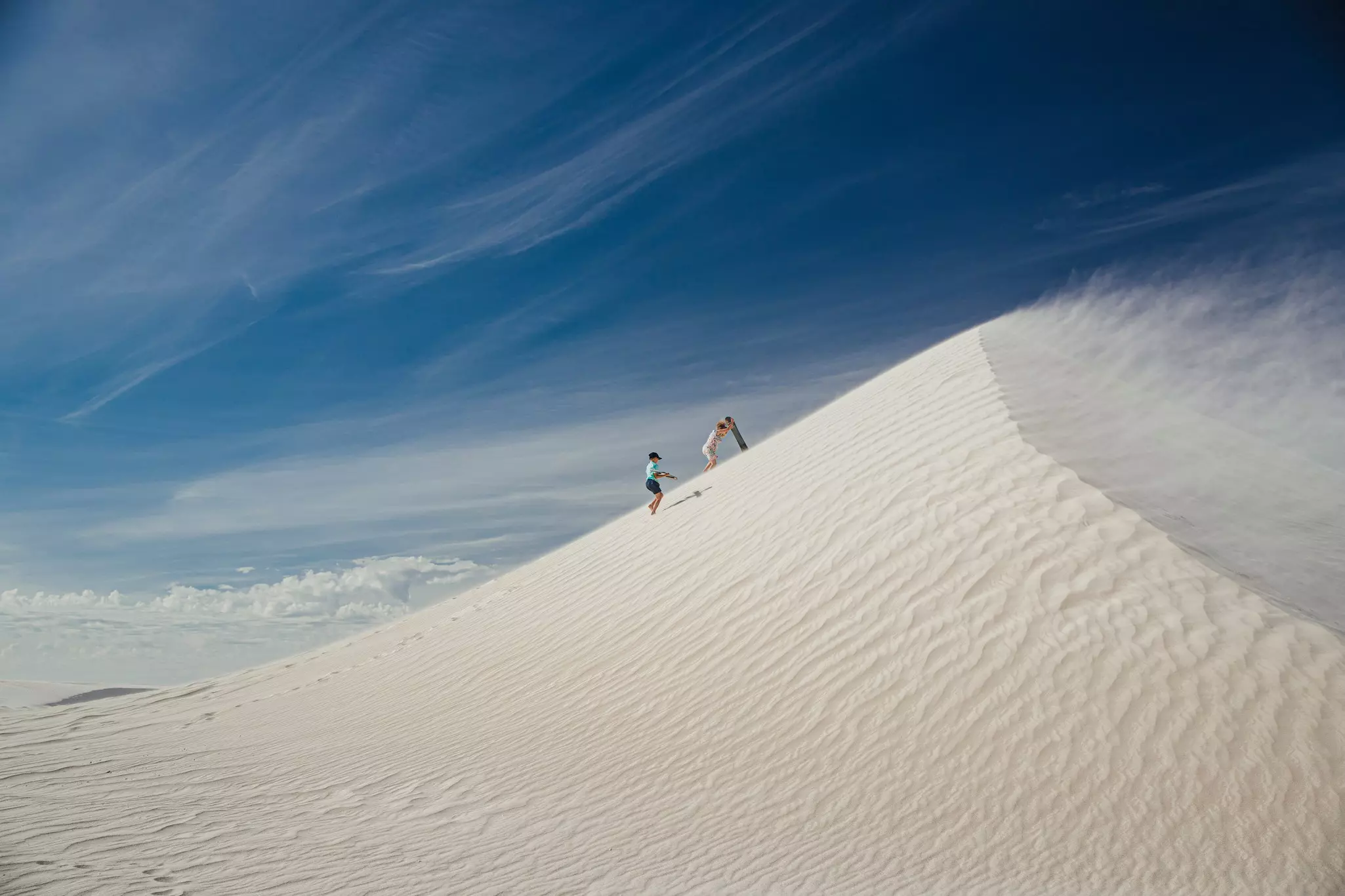 Wide angle view of a young boy and his mother climbing a sand dune at Lancelin Dunes. They are climbing up with sand boards, ready to sandboard down the dune.