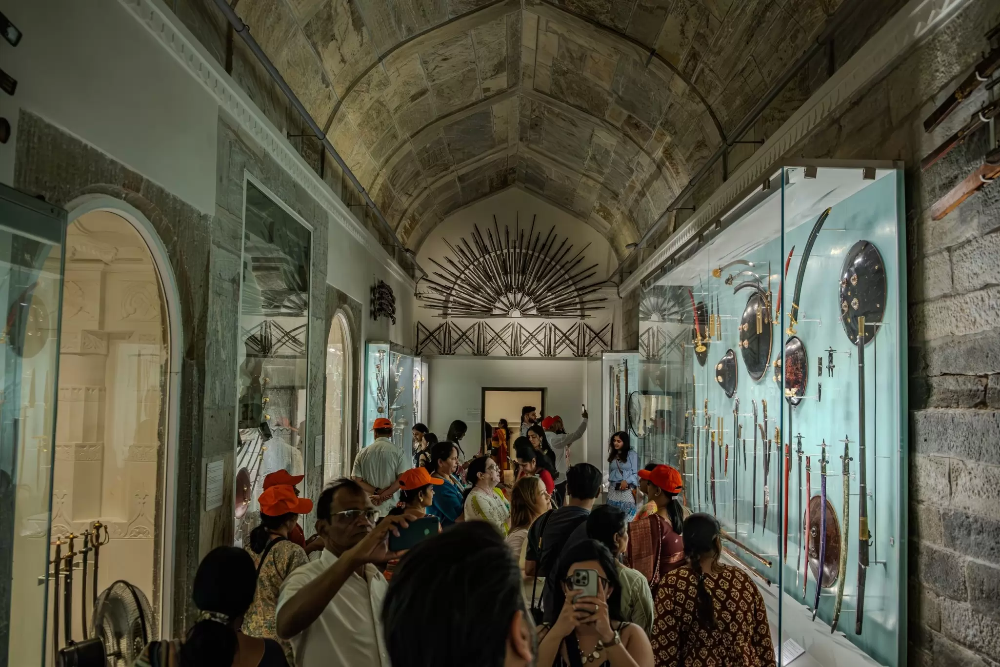 People hold up their phones to take photos of artifacts behind glass walls in a museum hall in Udaipur, India.