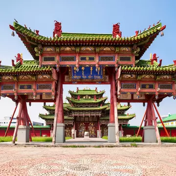 Red wooden gate with green tiled roofs at the Bogd Khan Winter Palace in Ulaanbaatar, a tiered temple seen through its arch