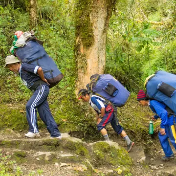 Peruvian porters with loaded packs carrying camping gear for hikers on the Inca Trail
