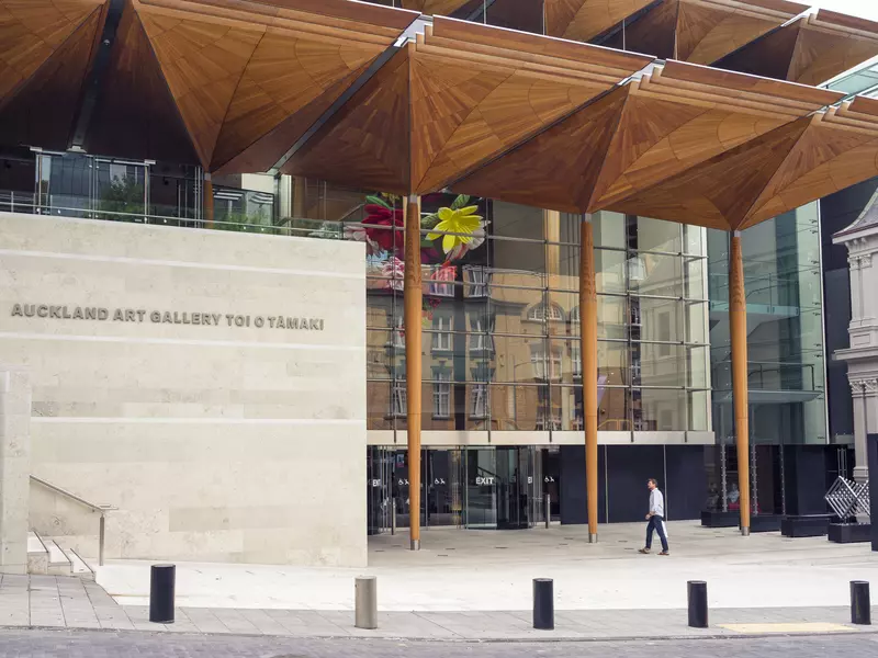 A man walks on concrete walkway toward the exterior of a building of stone and glass.