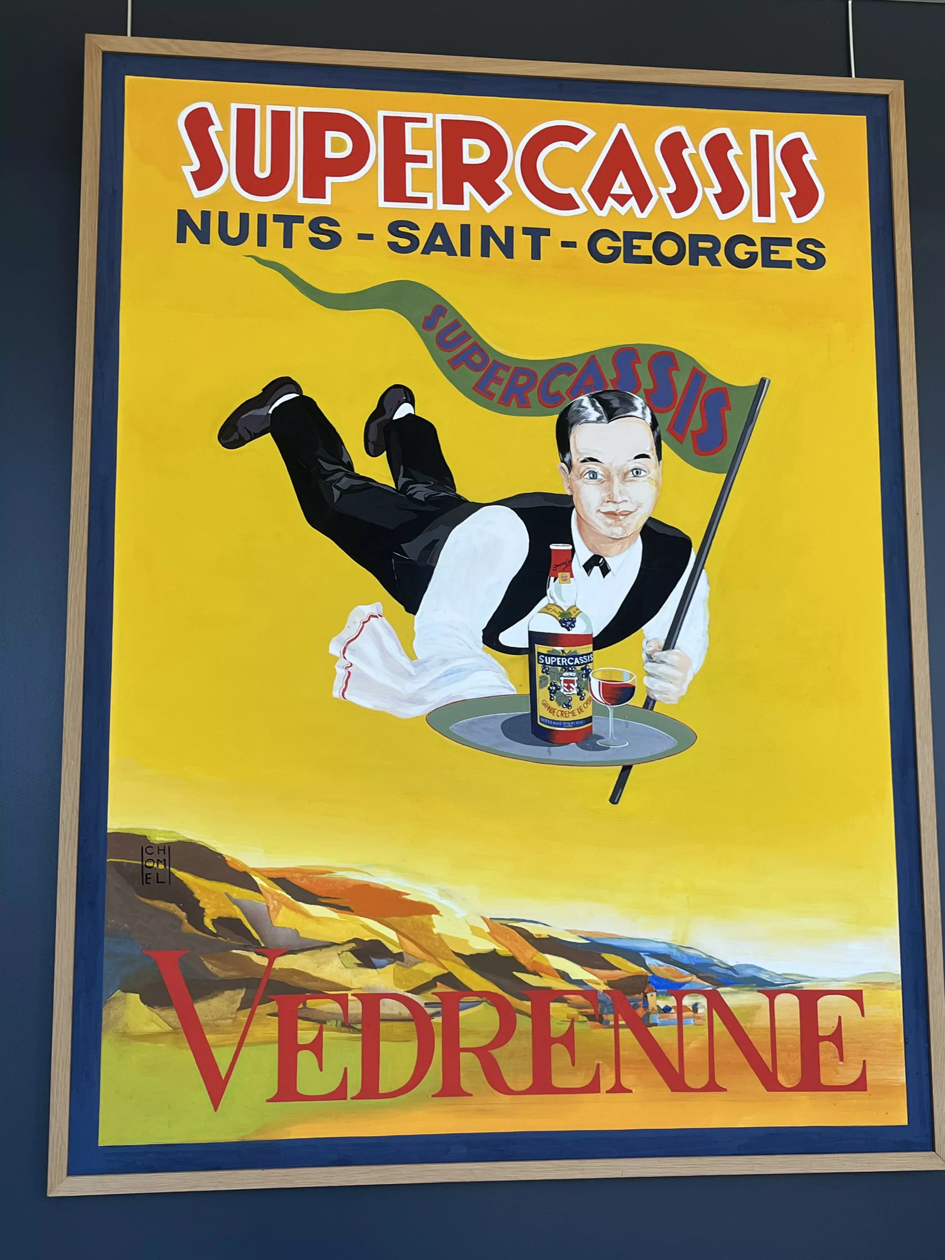 A cartoon on a poster of a man dressed as waiting staff flying through the sky holding a tray with a glass and bottle of blackcurrant liqueur